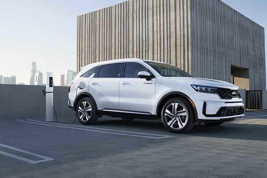 white Kia Sorento Plug-in Hybrid parked on a public rooftop, plugged into a charging station