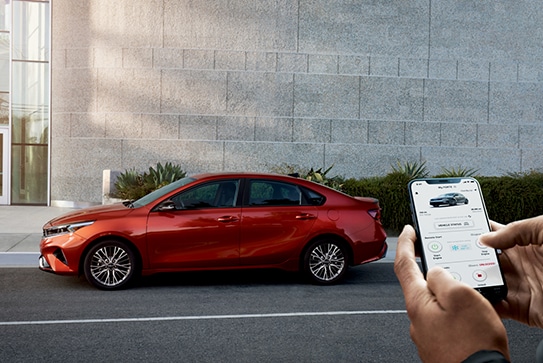 red Kia Forte sedan parked with driver starting it via an app