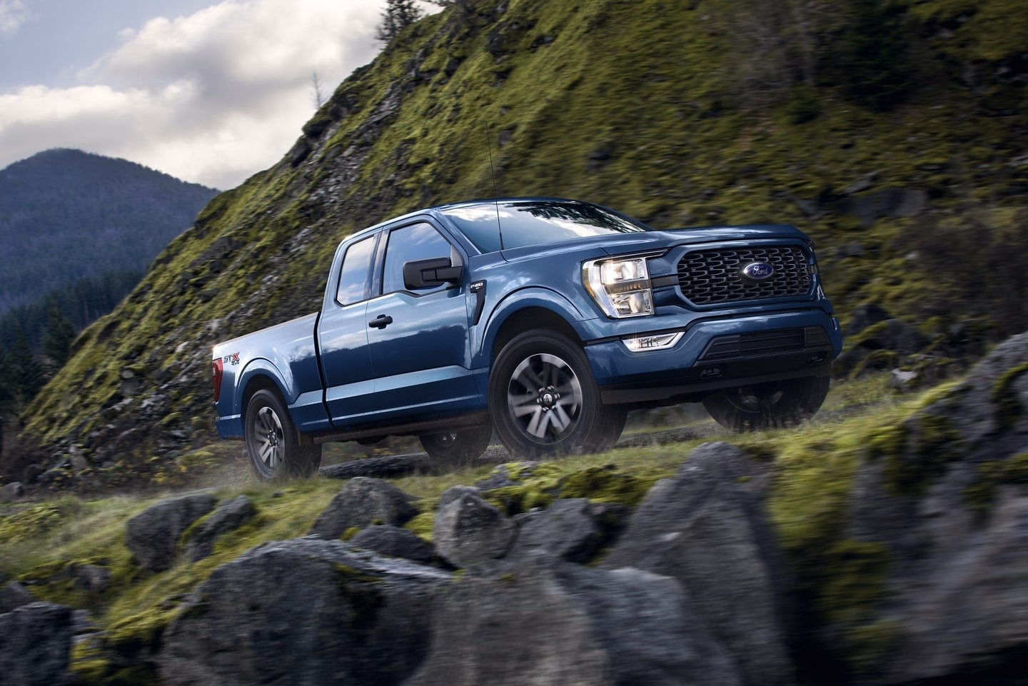 blue Ford F-150 truck driving fast up a dirt trail along a mountainside