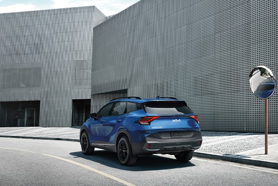 blue Kia Sportage parked next to a modern, grey building