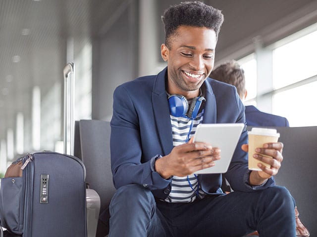 A smiling person sitting in a chair looking at a tablet device.