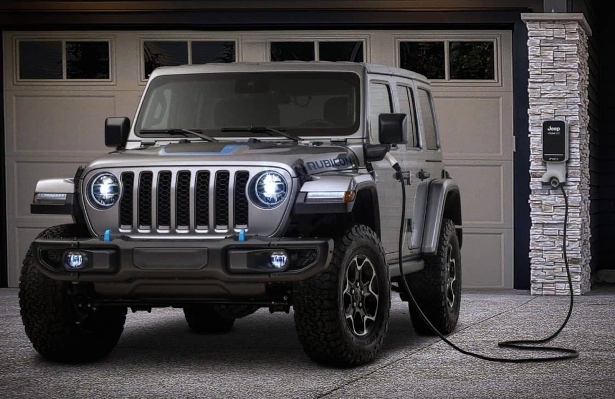 grey Jeep Wrangler 4xe hybrid SUV parked in front of a home, connected to a charging station