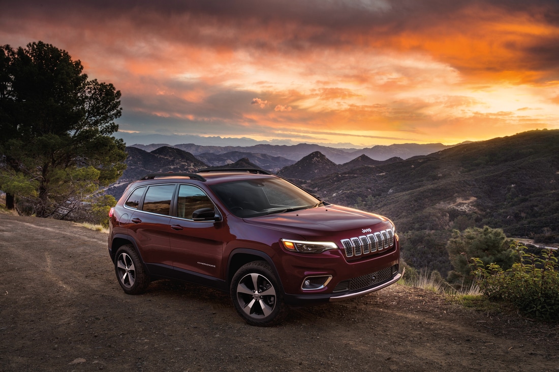 dark red Jeep Cherokee SUV parked in front of a sunset