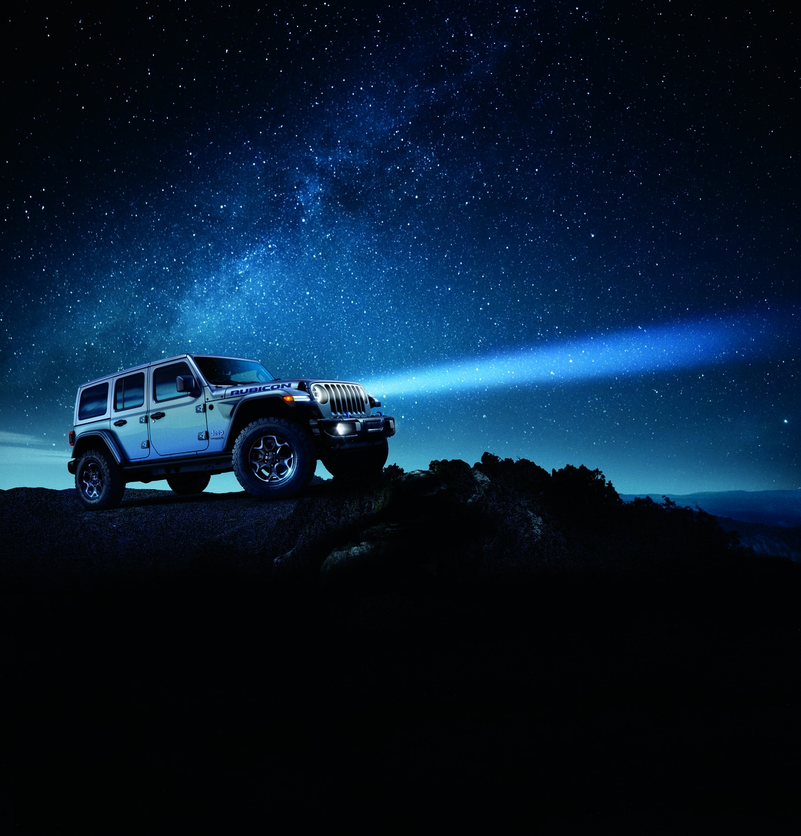 silver Jeep Wrangler Rubicon SUV parked on a rock under a very starry night sky