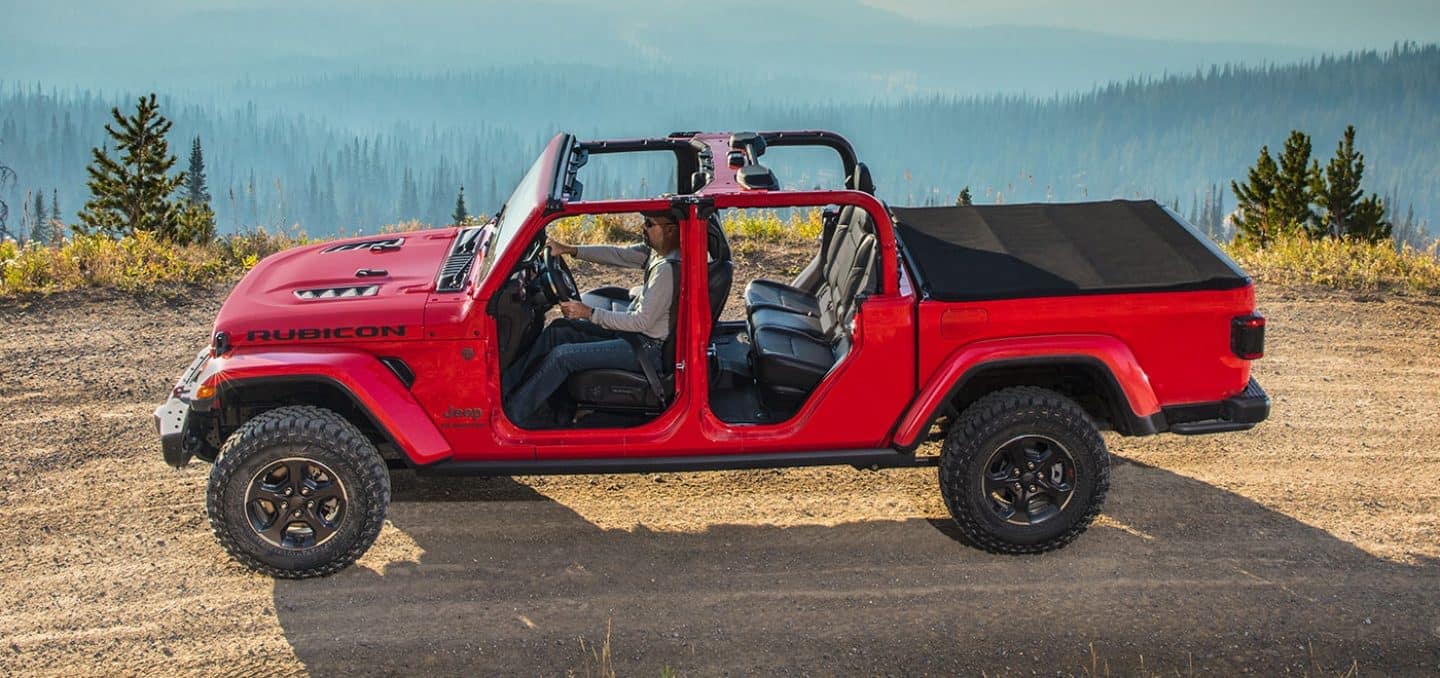 red Jeep Gladiator truck parked on a flat mountain area with the doors and roof removed