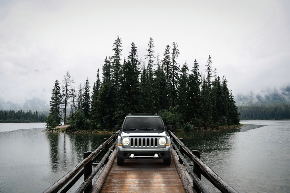 silver Jeep Patriot parked on a bridge with a forest in the background