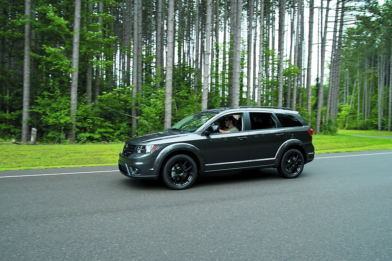 dark gray Dodge Grand Caravan driving on a wooded highway