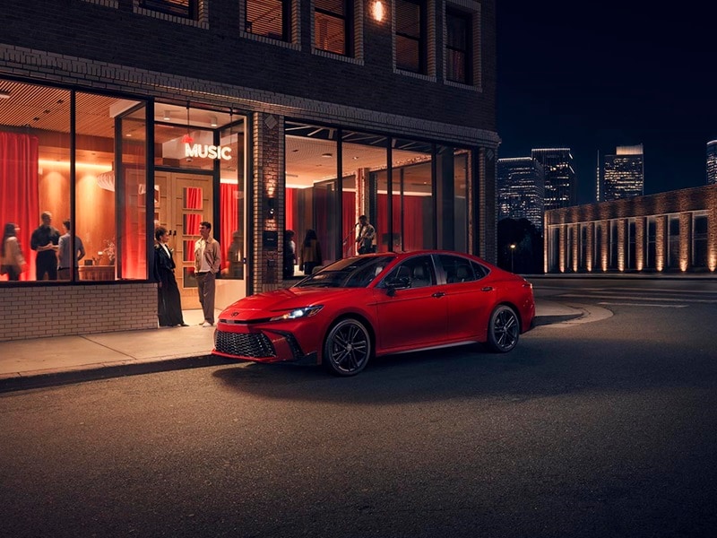 A red 2026 Toyota Camry is parked outside of fancy restaurant with people standing around