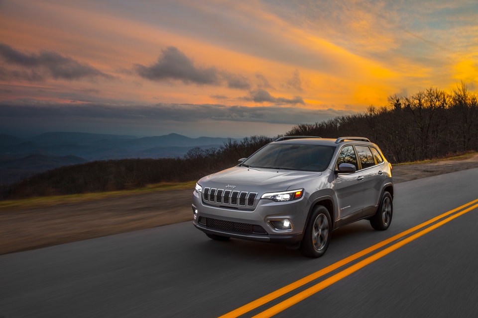 silver Jeep Cherokee SUV driving on a highway with the sunset in the background