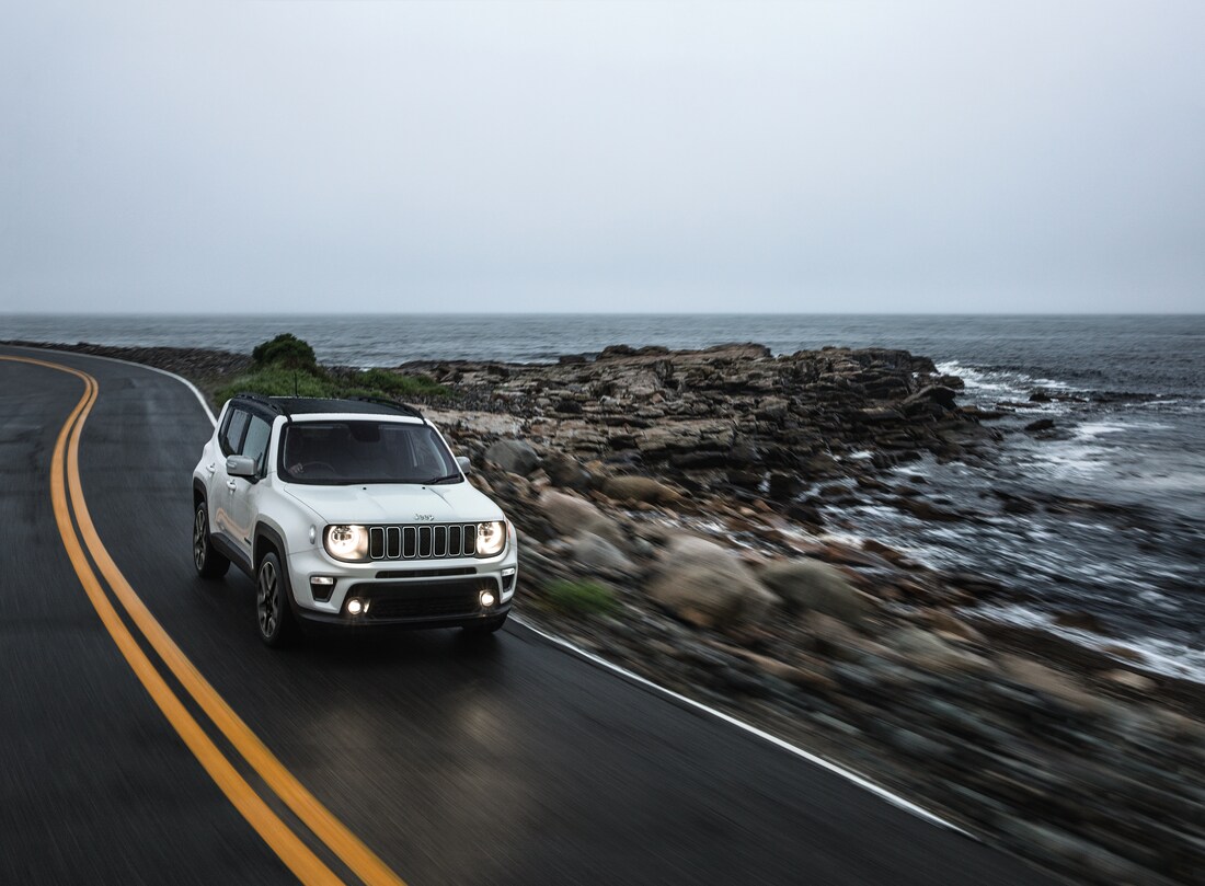 white Jeep Renegade SUV driving past a rock oceanfront
