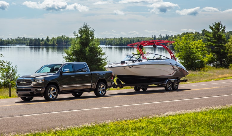 black Ram 1500 truck towing a boat next to a lake