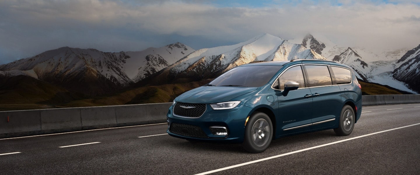 teal Chrysler Pacifica minivan driving down a highway with snowy mountains in the background