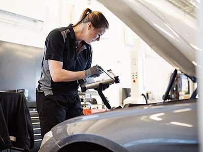 Service Technician Careers at Lithia Chrysler Dodge Jeep Ram FIAT of Roseburg Service Technician standing over a vehicle engine bay holding a clip board and inspecting the vehicle.