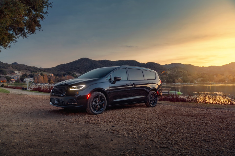 black Chrysler Pacifica minivan parked on a lakeside hill at sunset