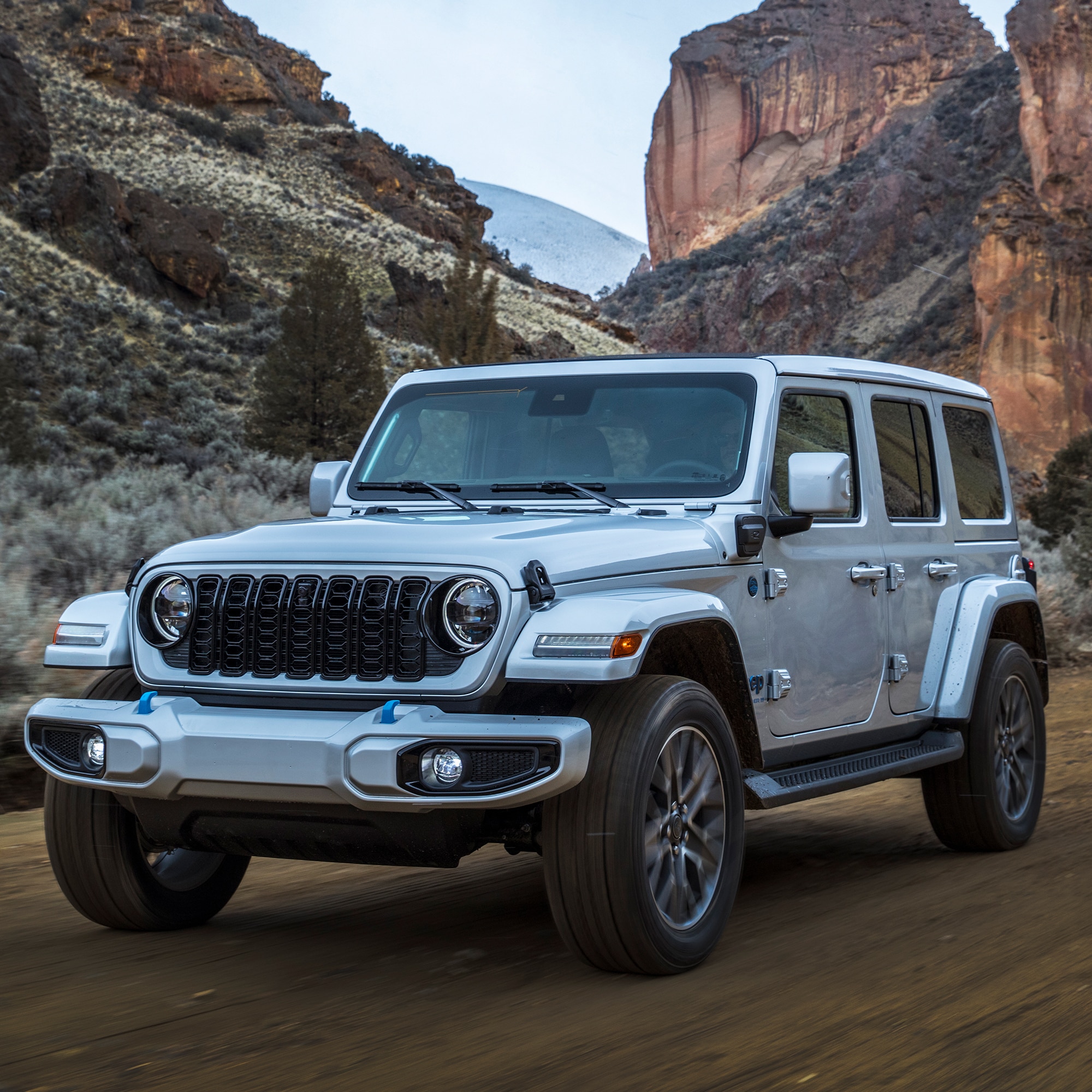 silver jeep wrangler 4xe parked among some large red rocks