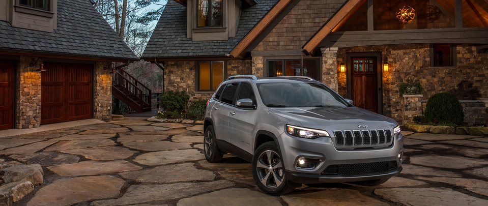 dark gray Jeep Cherokee SUV parked in front of a log cabin