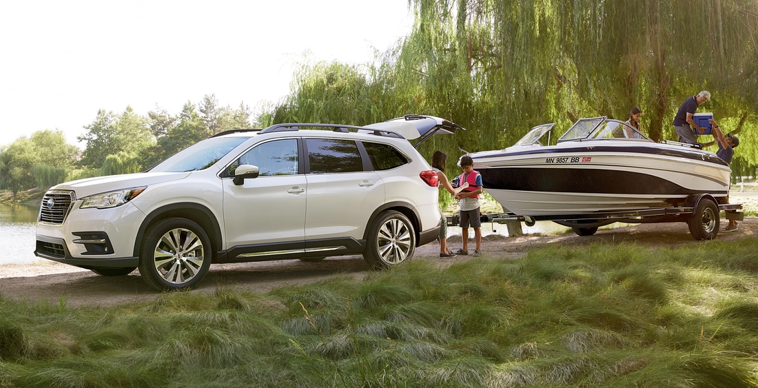 white Subaru Ascent Third-Row SUV towing a boat next to a river