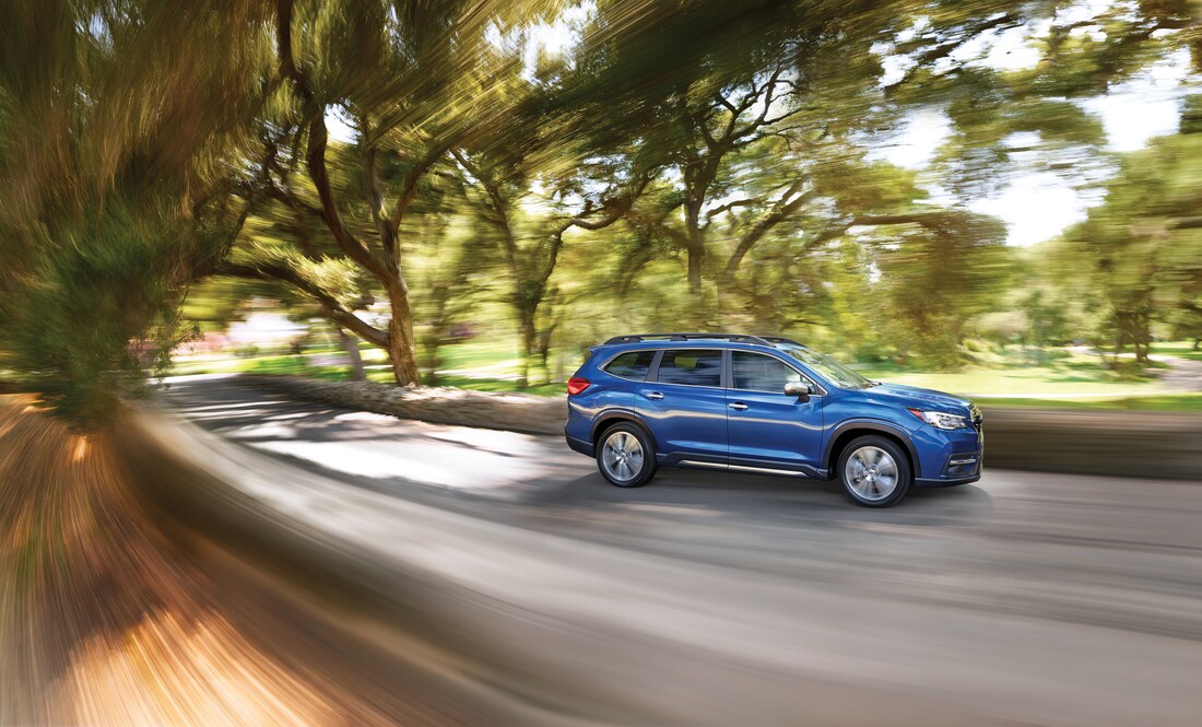 blue Subaru Ascent SUV heading around a corner with a blurred tree-lined street in the background