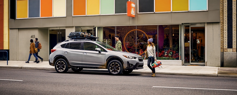 white Subaru Crosstrek crossover SUV parked in front of a modern art painted retail building