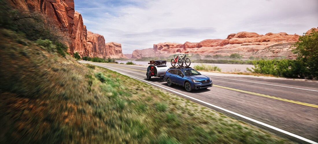 blue Subaru Outback SUV towing a teardrop trailer with biking and camping gear attached