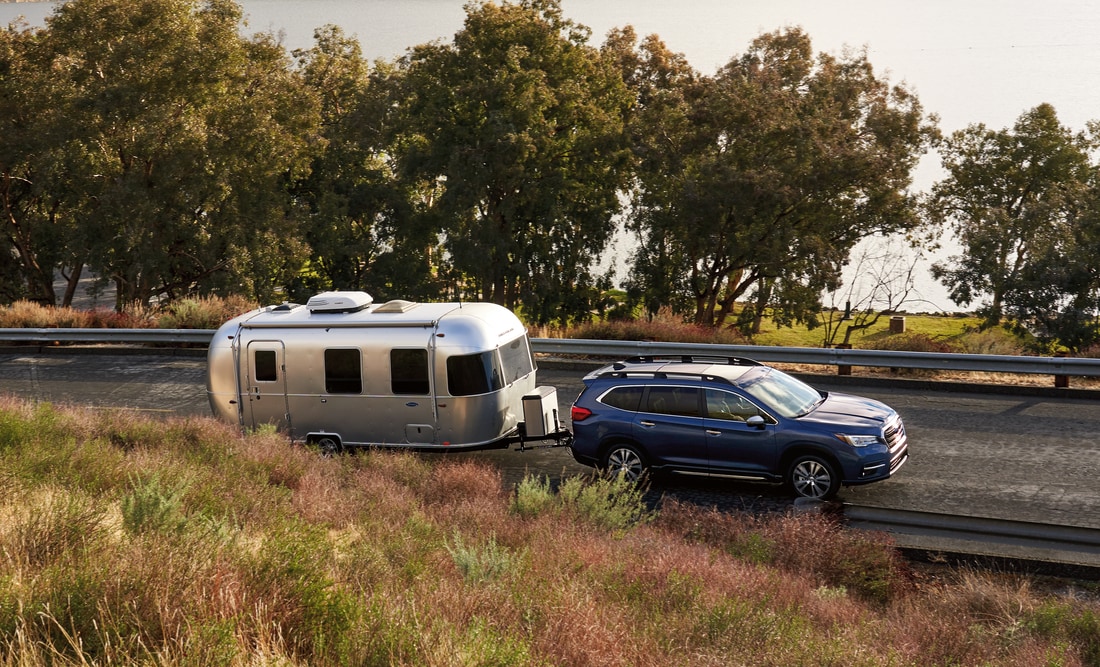 blue Subaru Ascent SUV driving along a waterway, towing an Airstream trailer