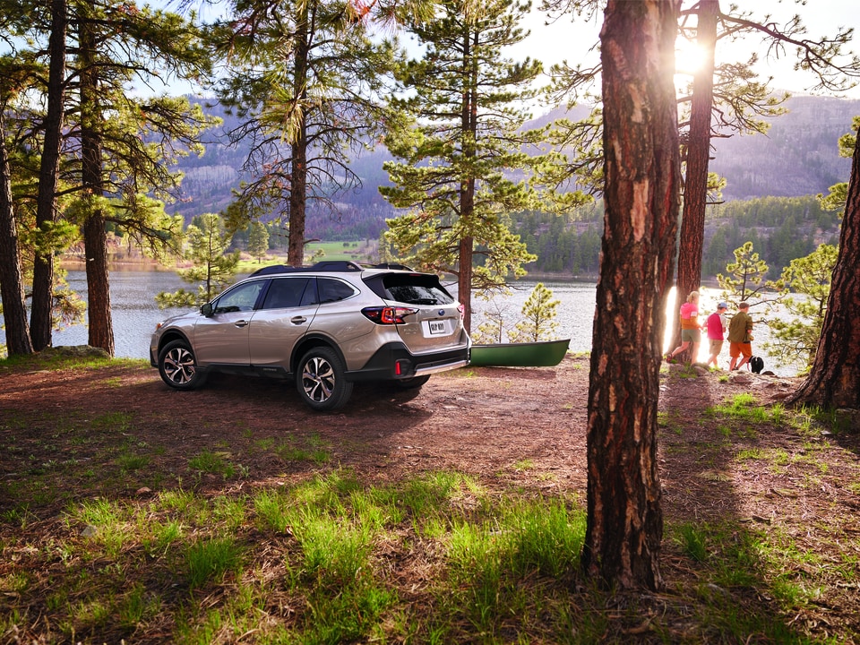 silver Subaru Outback parked under evergreen trees at a camping site