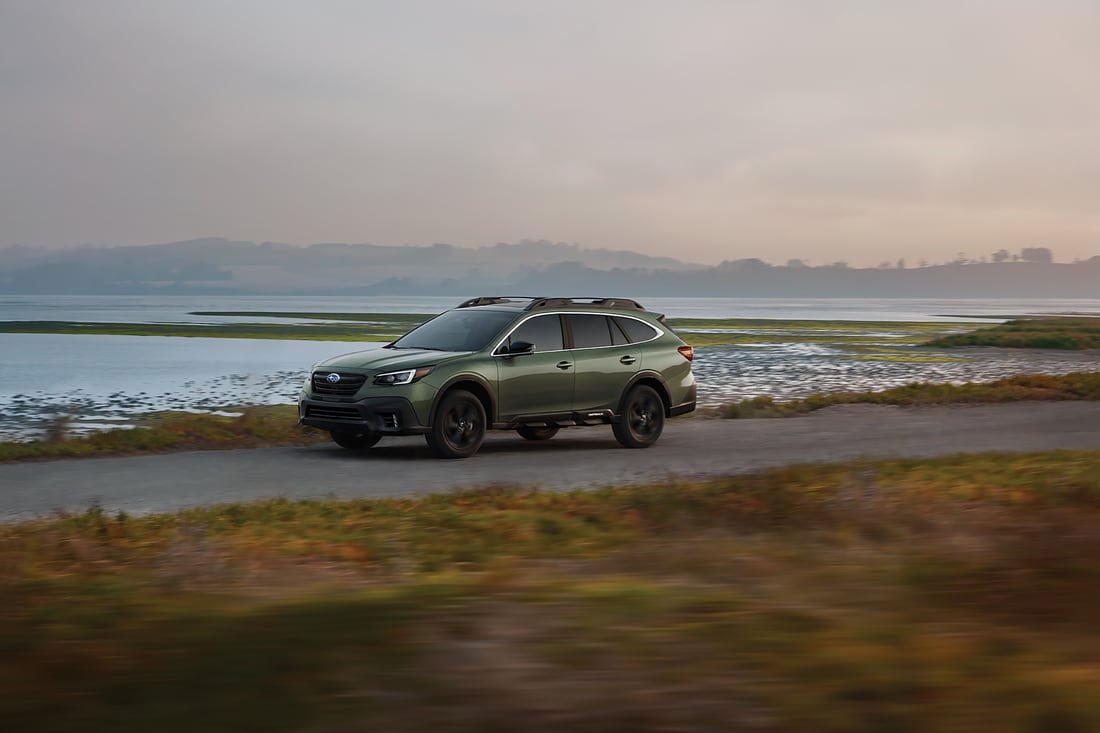 green Subaru Outback SUV driving past the beach