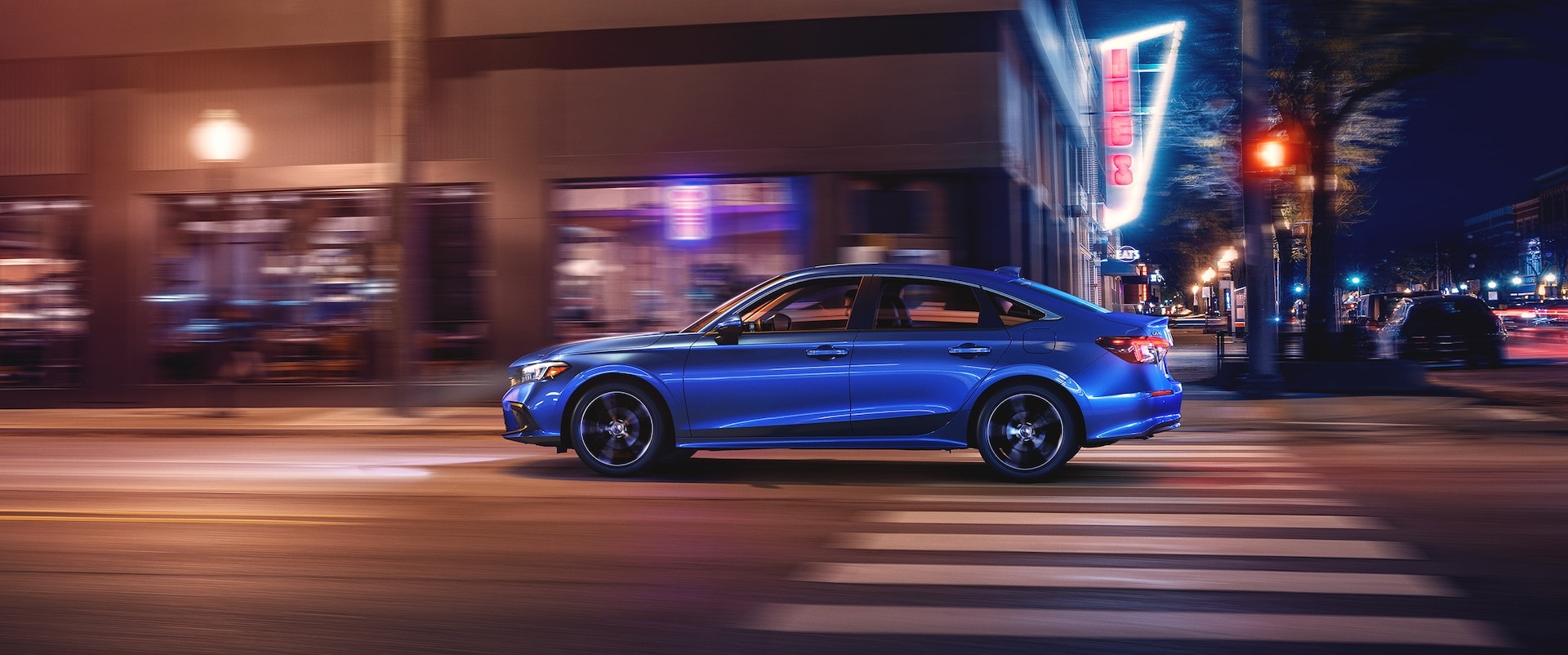 blue Honda Civic driving through a brightly lit city at night
