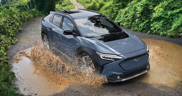 2022-Subaru-Ascent-Touring-SUV-L02.png blue Subaru Ascent SUV driving fast around a corner with blurred background