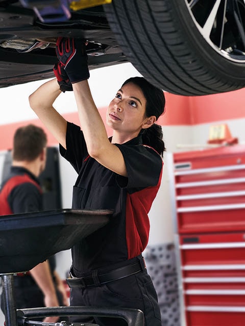 A Toyota service technician standing under a vehicle performing an Oil Change.