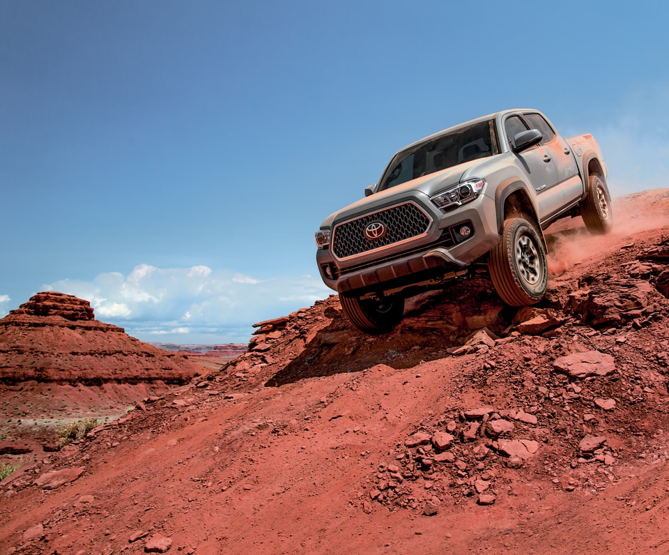 gray Toyota Tacoma truck climbing down a steep, red desert hill