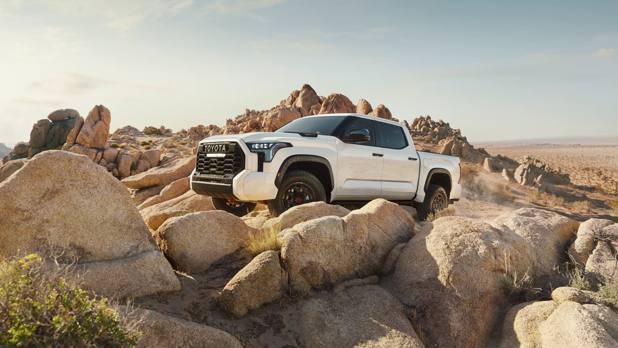 white Toyota Tundra truck bouldering over some large rocks