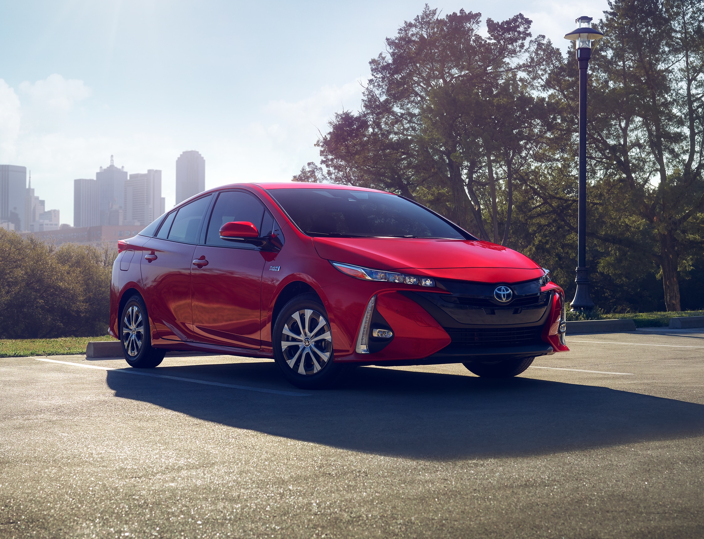 red Toyota Prius parked in a lot with a city in the background