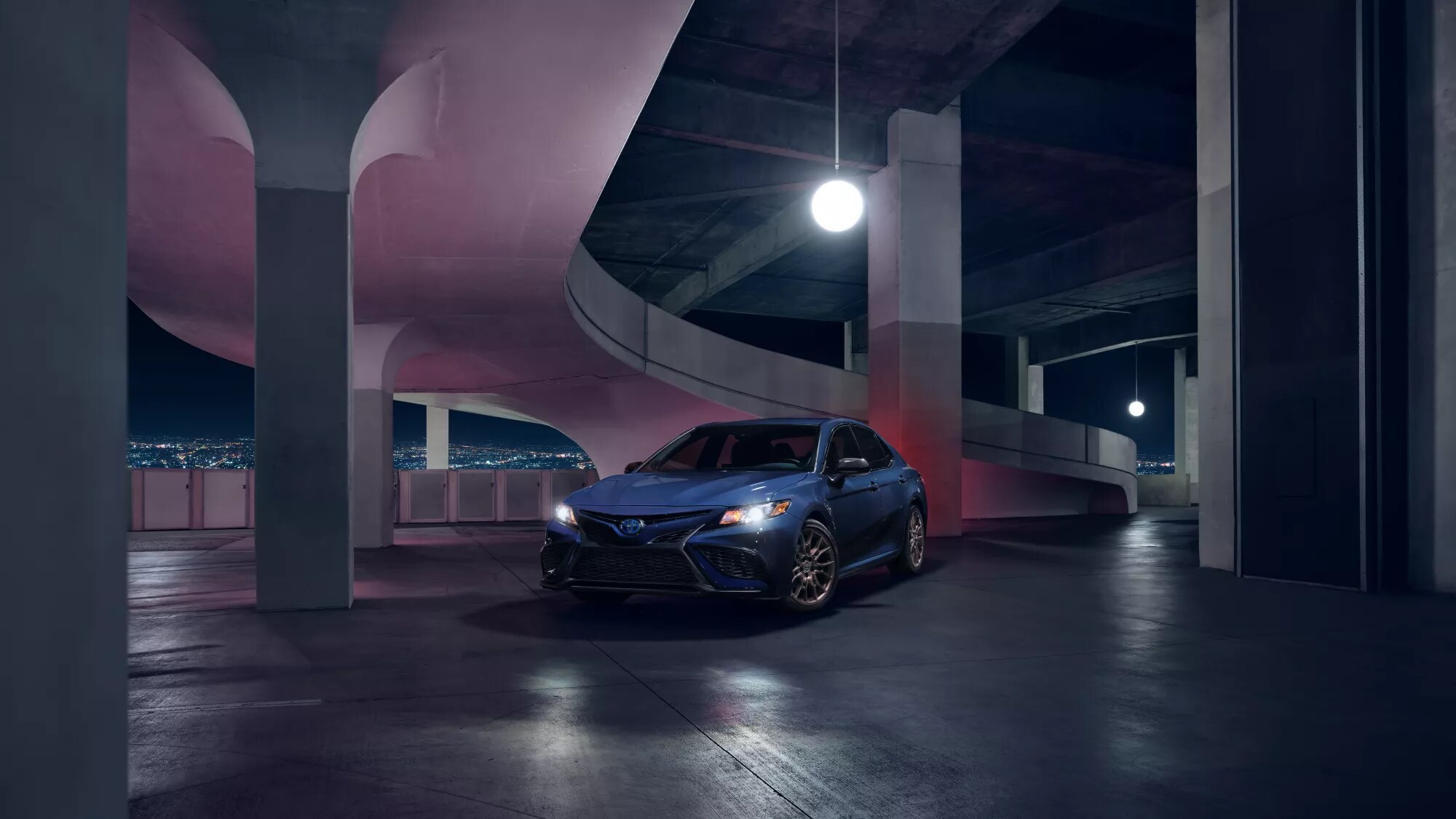 blue Toyota Camry Hybrid driving through a car park at night
