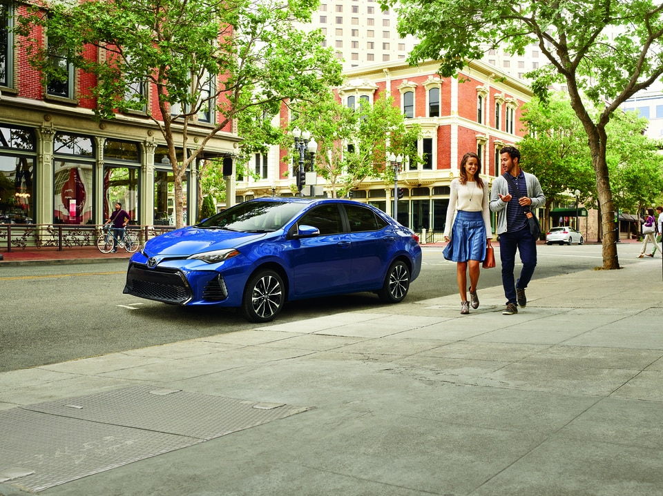 blue Toyota Camry parked on a downtown city street, next to a brick building