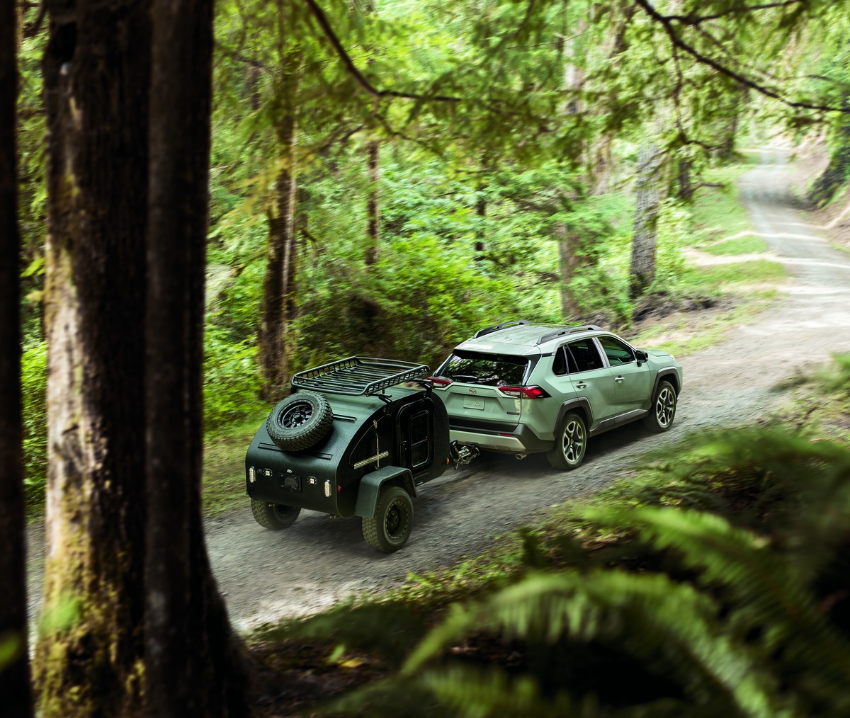 silver Toyota RAV4 SUV towing a teardrop trailer through the woods