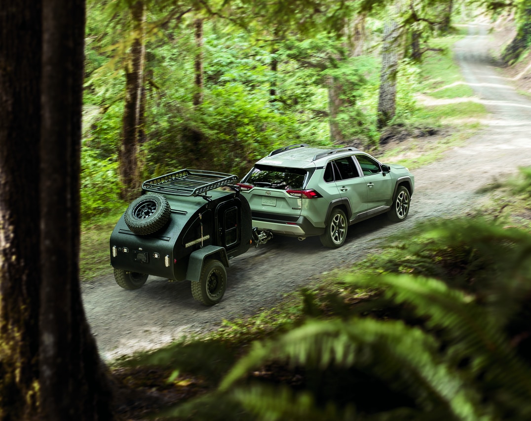 silver Toyota RAV4 SUV driving on a forest trail, towing a teardrop trailer