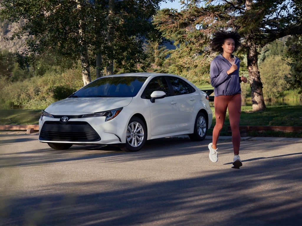 white Toyota Corolla hatchback parked with the driver jogging nearby