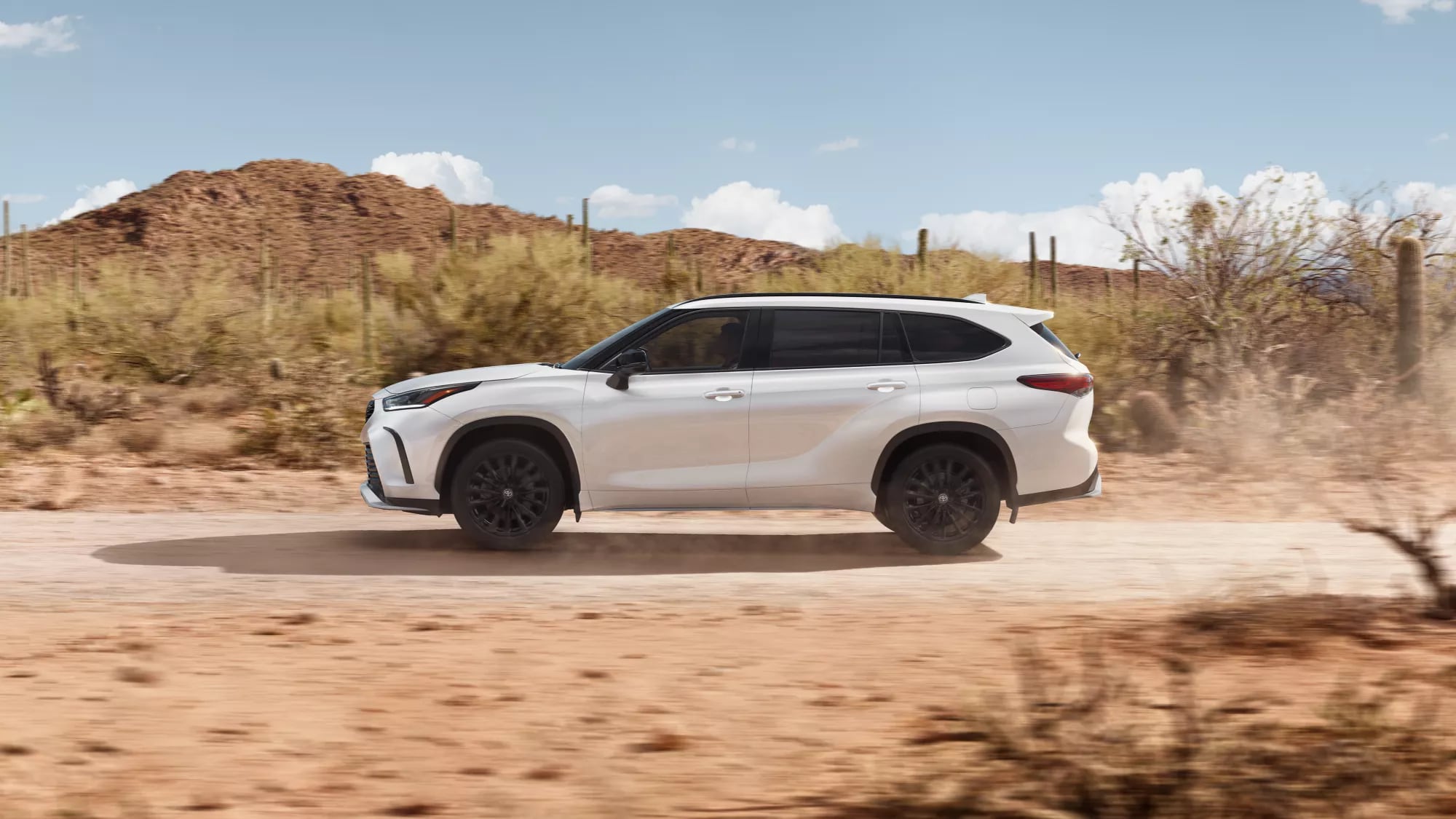 white Toyota Highlander SUV driving fast through a desert area