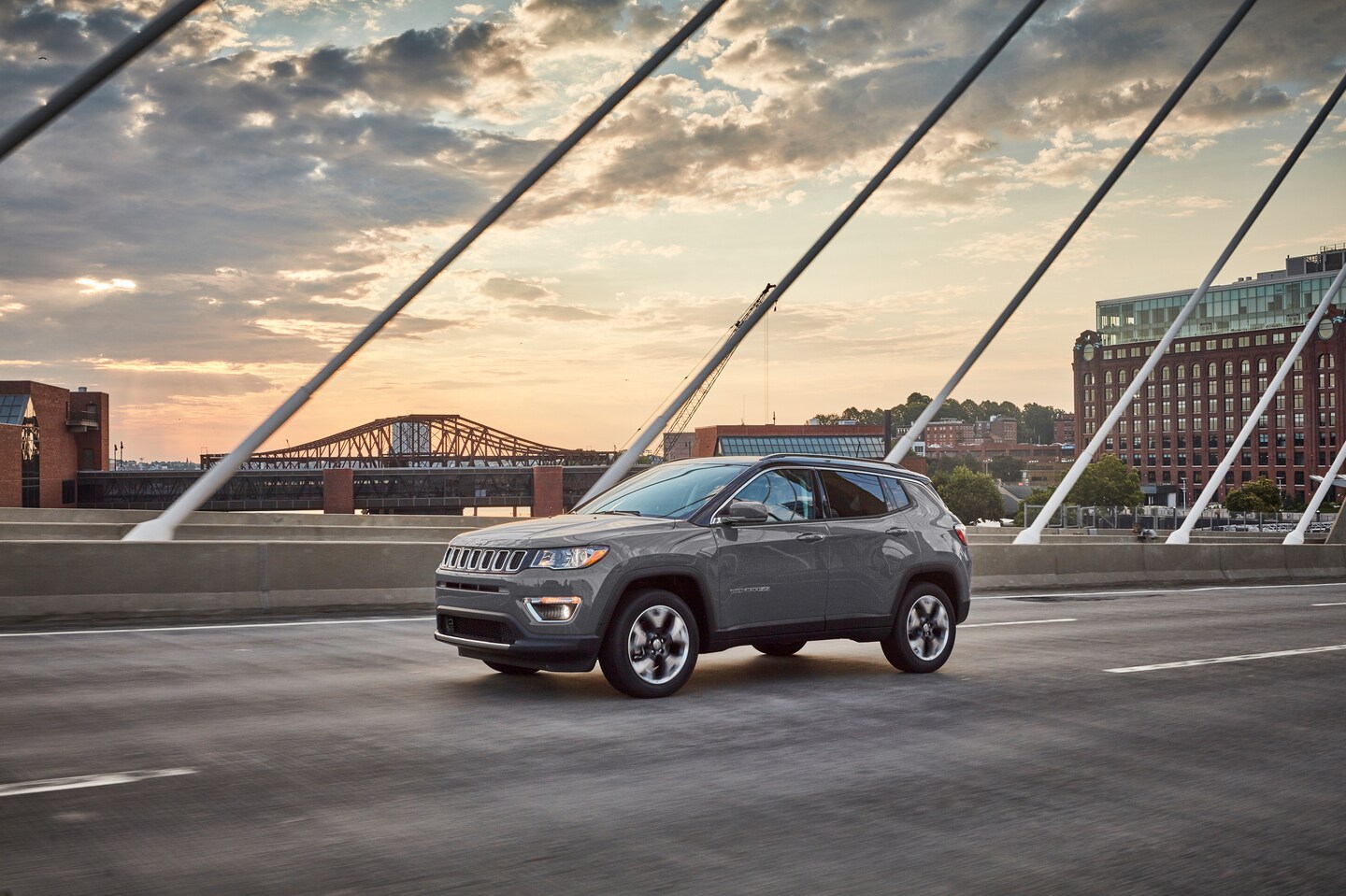 grey Jeep Compass driving on a bridge, through a city with industrial brick buildings