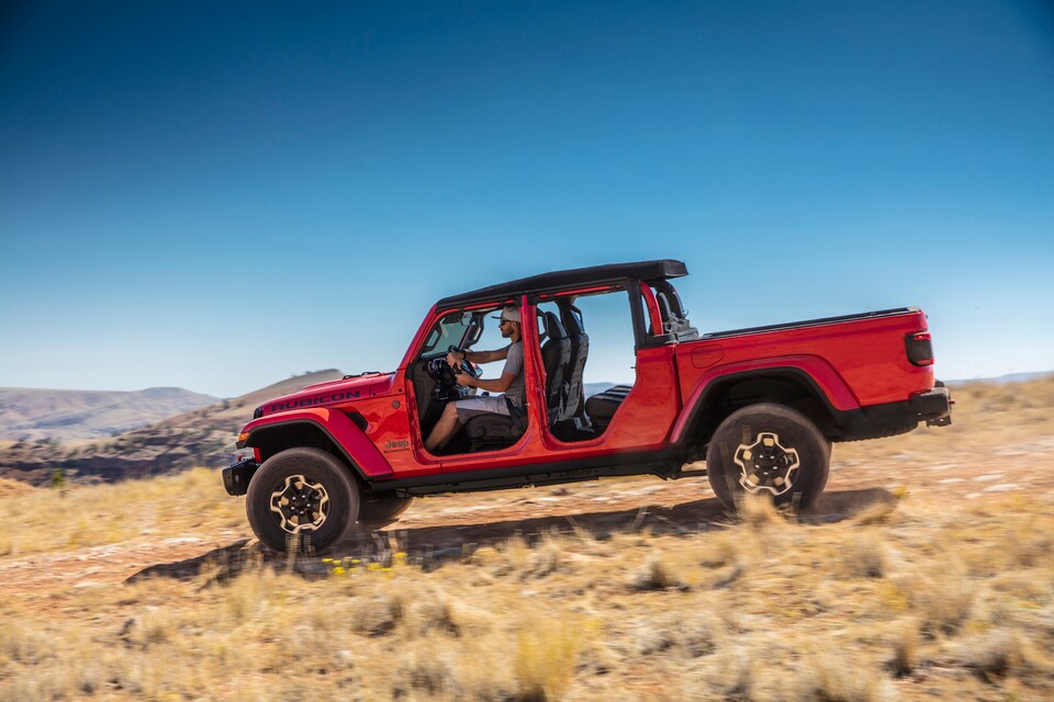 red Jeep Gladiator truck driving through the desert with the doors off