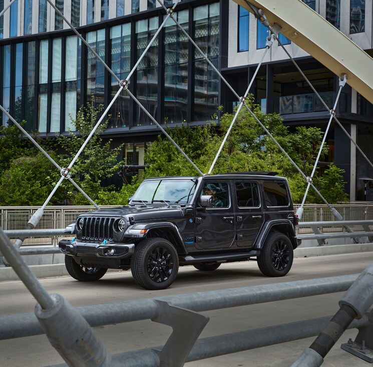 2025-Jeep-Wrangler-Sport4xe-SUV-L.png dark grey Jeep Wrangler 4xe driving on a bridge
