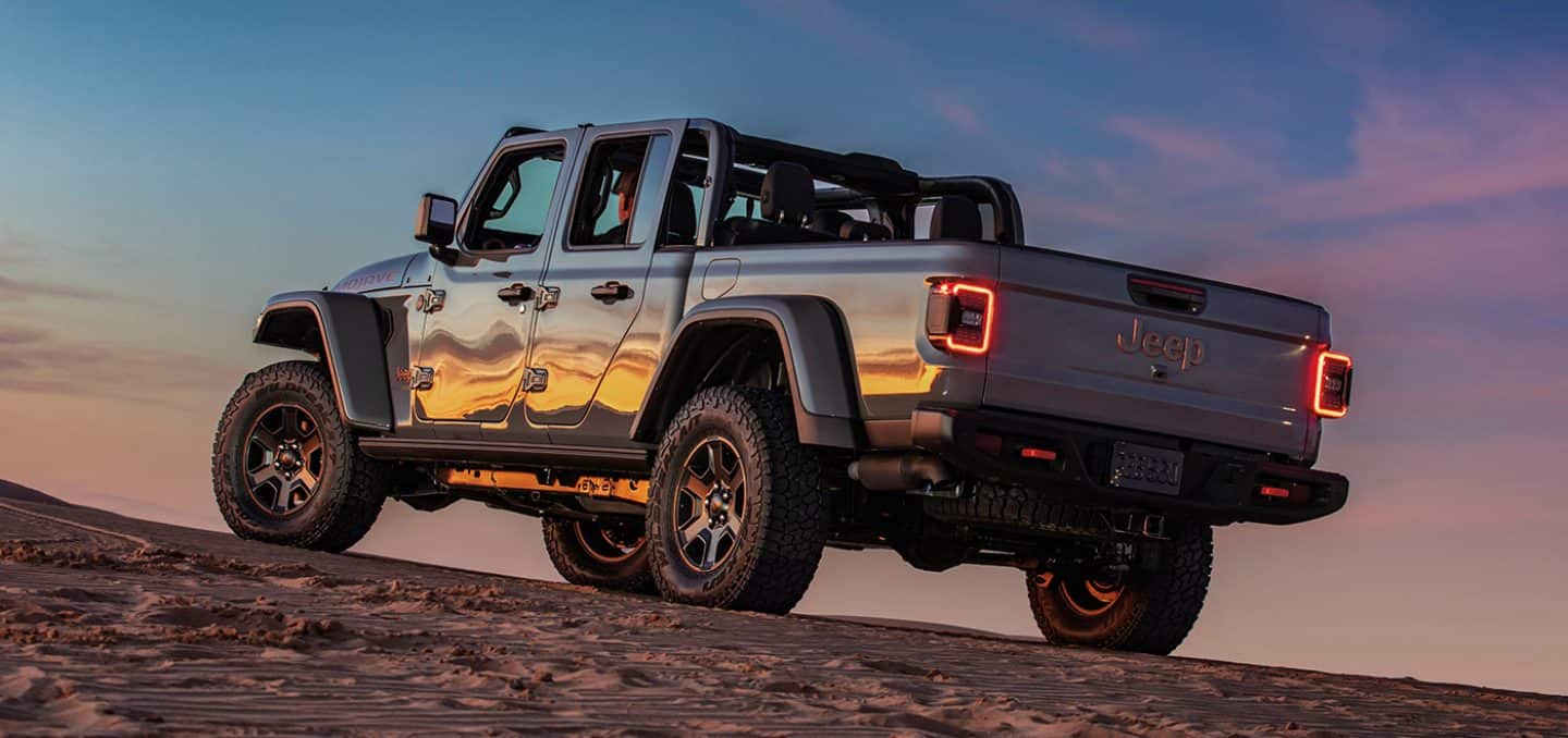silver Jeep Gladiator truck climbing up a steep cliff at sunset