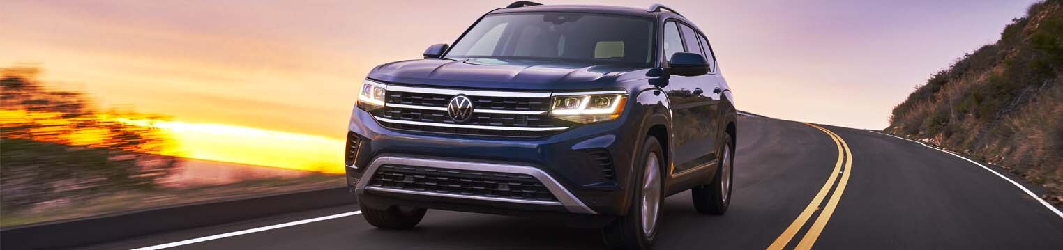 2021 Volkswagen Atlas driving on a road with a sunset behind it.