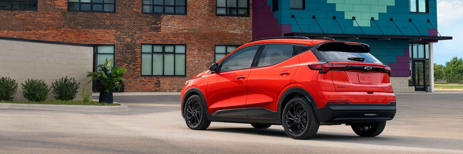 Red 2027 Chevrolet Bolt parked on a in front of a brick building