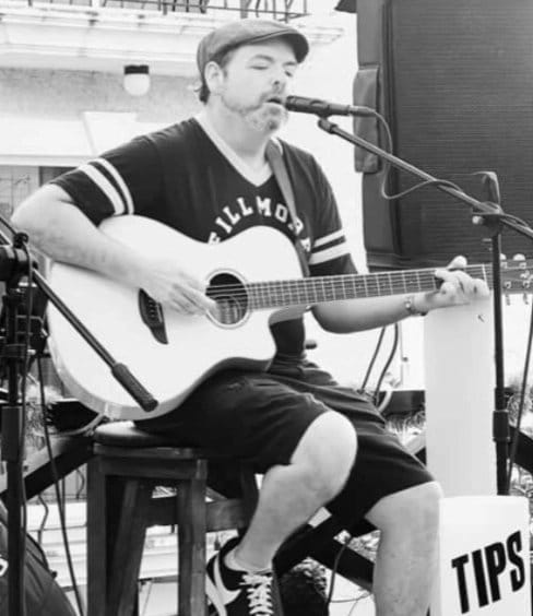 Picture of Edward Barnett playing an acoustic guitar and singing.