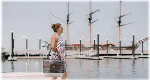 Mary walking Newport harbor with one of her upcycled bags. there are boats in the background.
