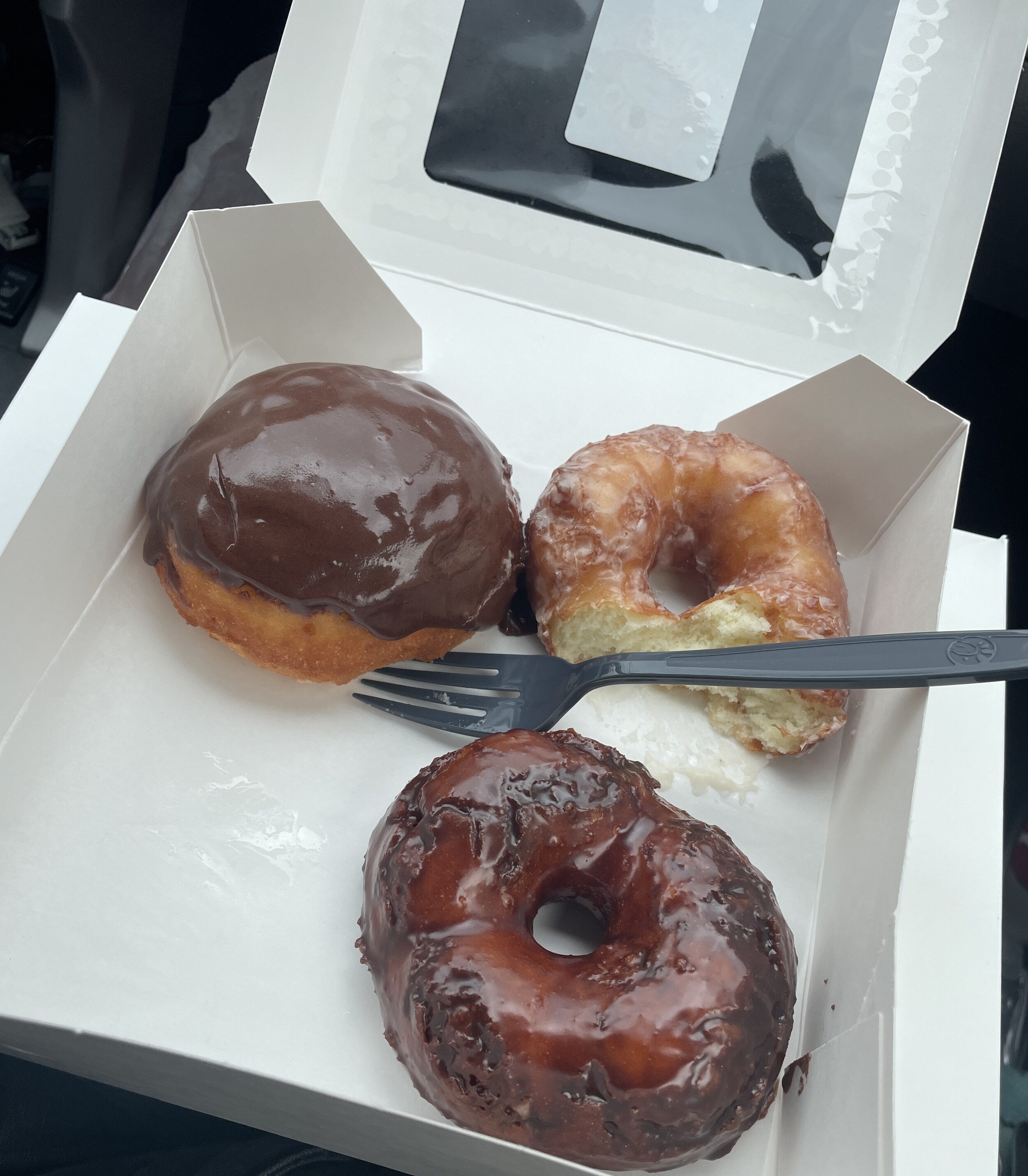 3 donuts from okie dokie donuts. one is a boston cream, the other is a maple glazed and then a chocolate glazed donut. 