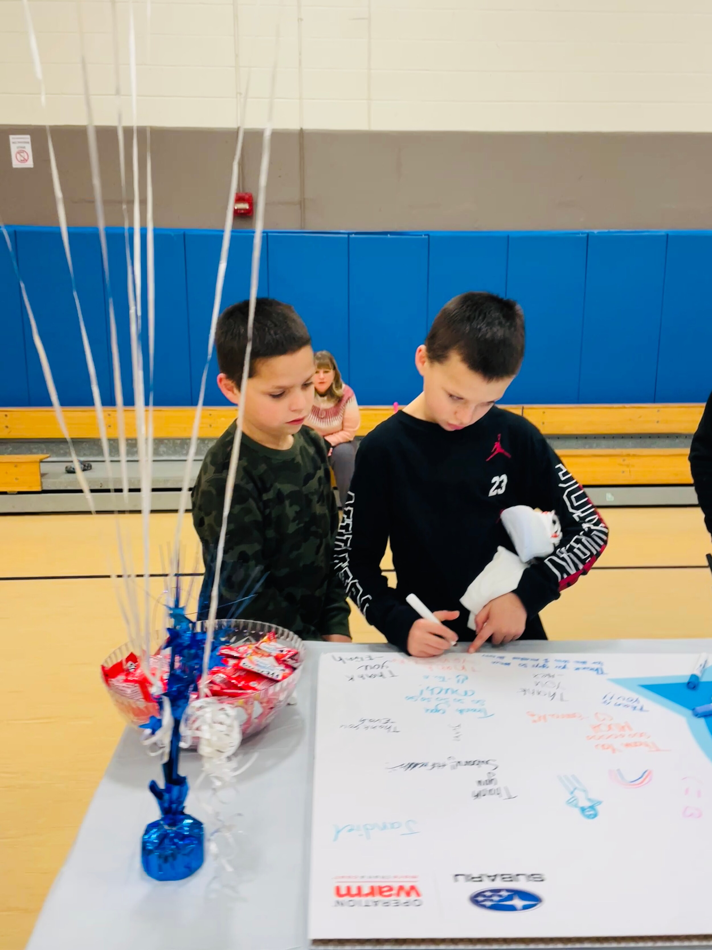 2 twin boys in black shirts writing thank you notes on a poster board for Long Subaru.