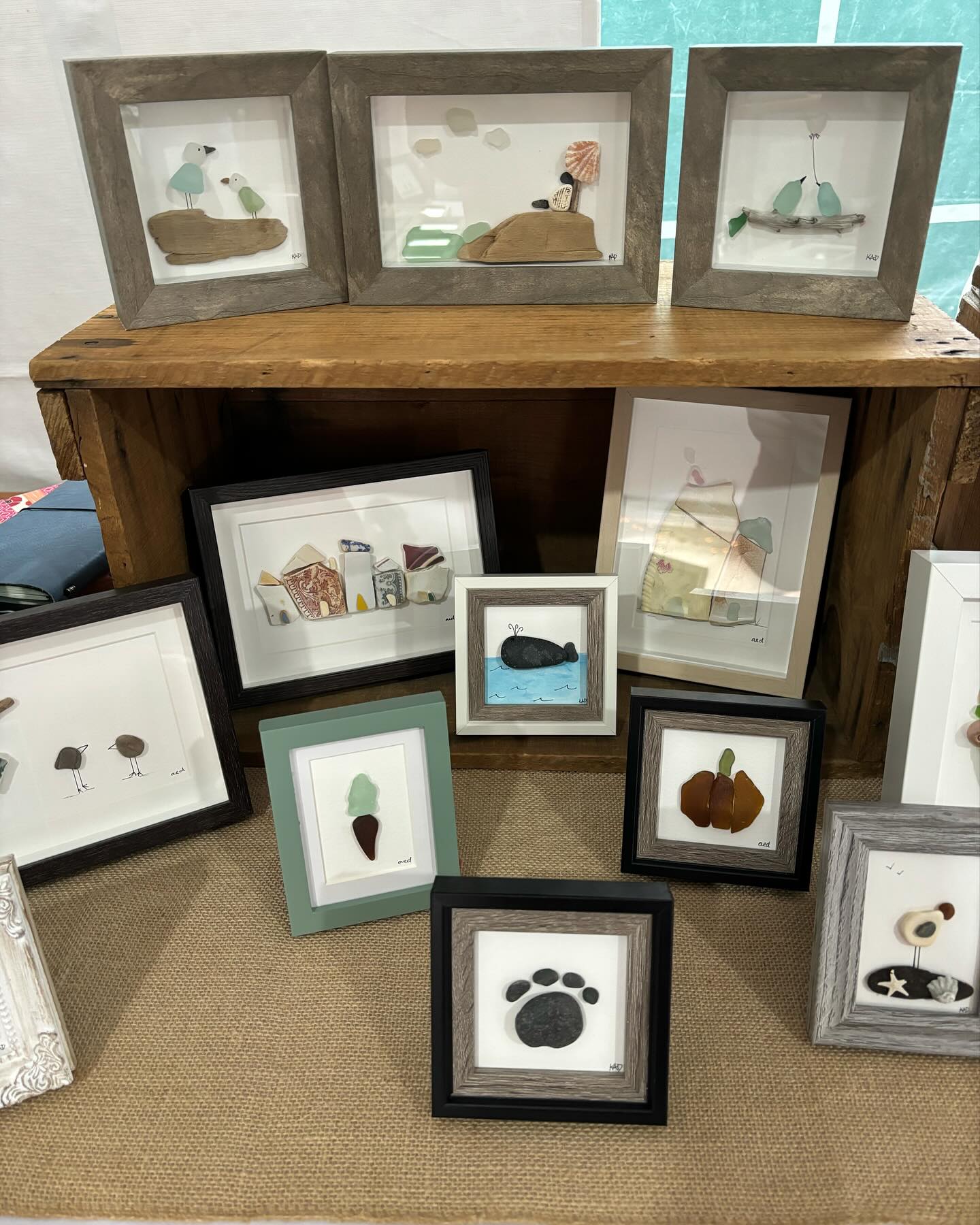 a bunch of framed art created from beach rocks, shells, and sea glass. 